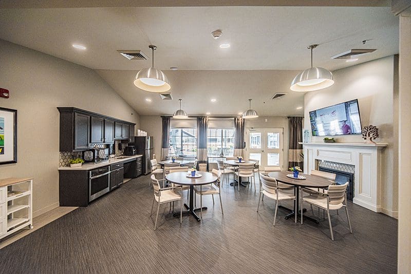 Multipurpose activity room at Charter Senior Living of Paducah, KY, featuring a kitchenette, fireplace, and casual dining tables for resident programs and gatherings.